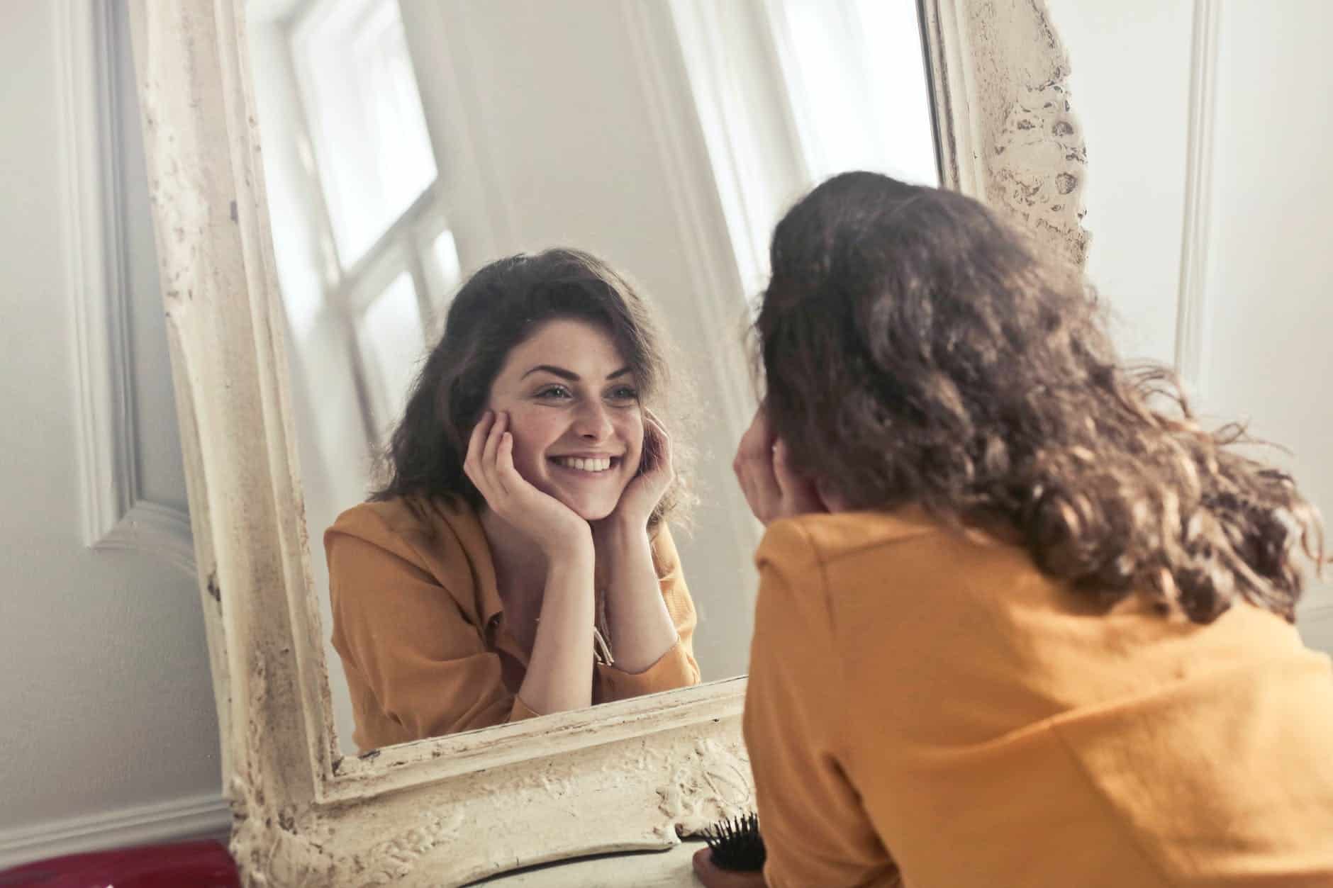 a woman smiling at herself in the mirror, showing optimism. an example of how sports psychology and the role of visualisation can improve sports performance