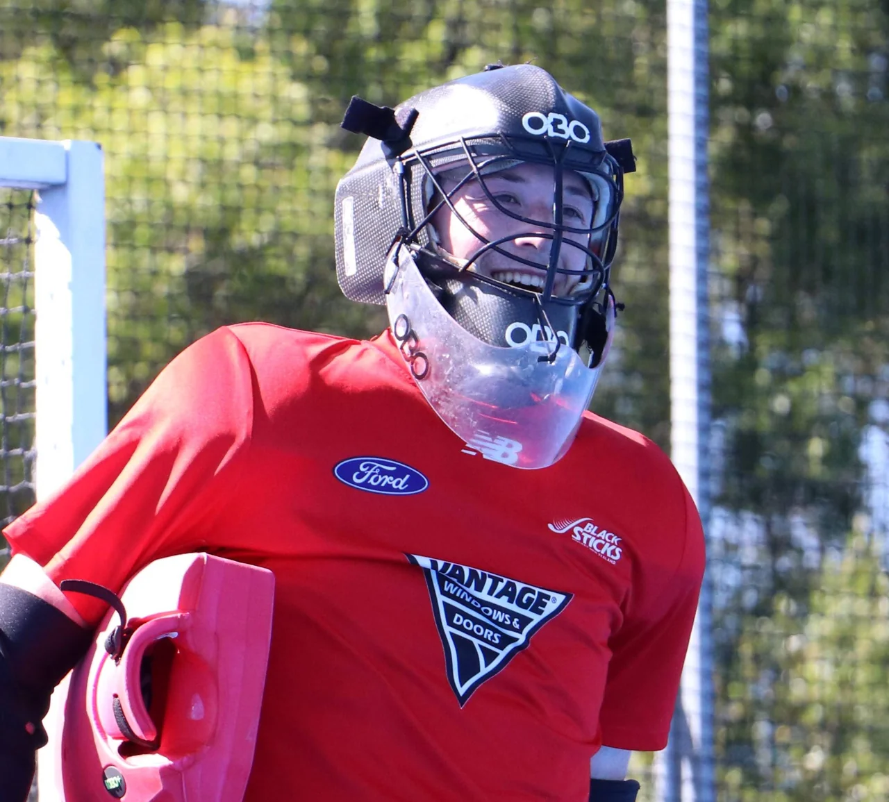 Field hockey goalkeeper in a red playing shirt and protective helmet